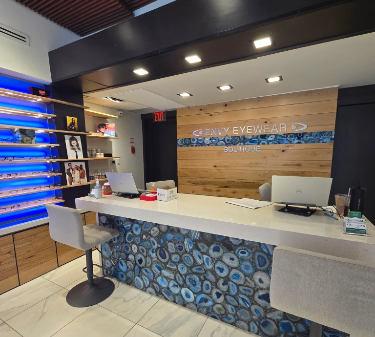 Envy Eyewear Boutique storefront interior featuring a reception desk and eyeglass display wall with backlit shelving.